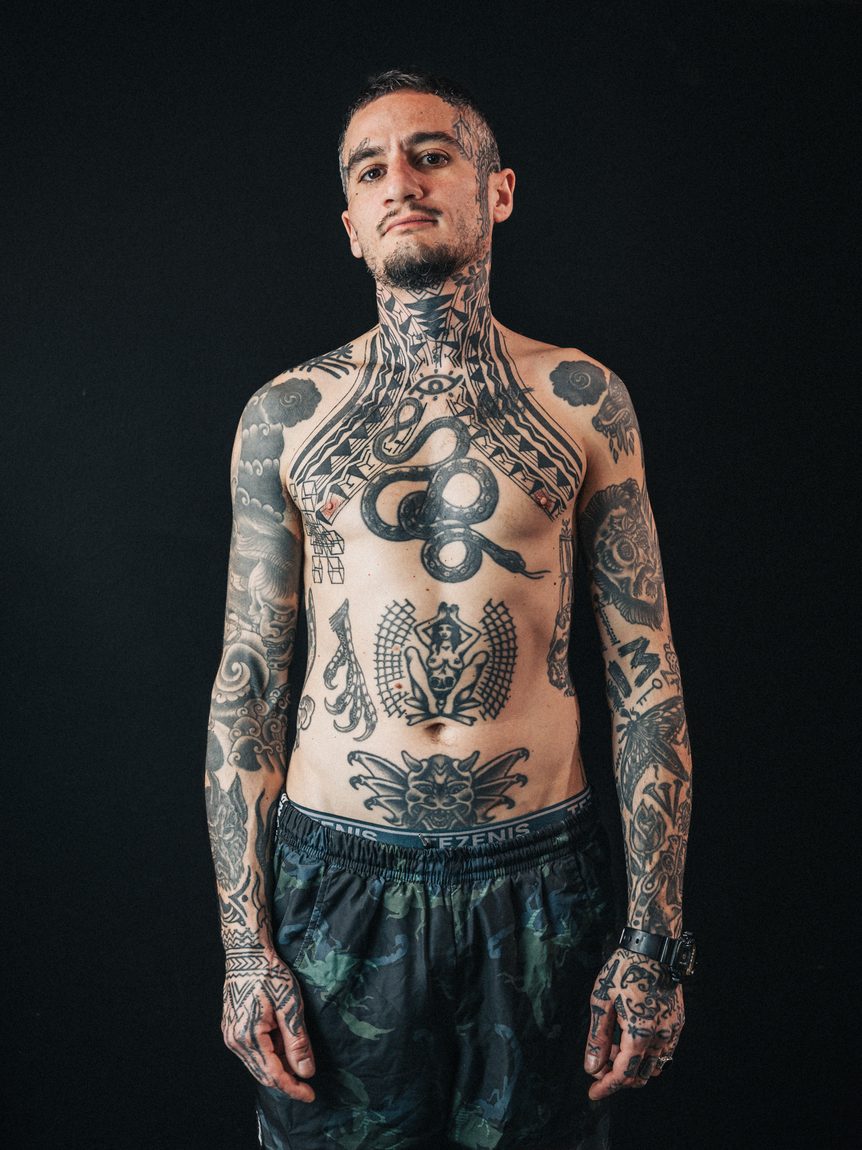 Il corpo tatuato, in posa contro il fondo scuro. Bodymarkings, Bologna.